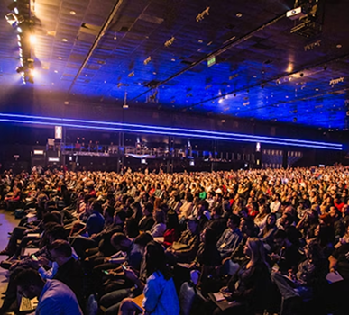 Wide shot of a packed conference hall with stage lighting during a keynote session